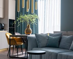 Comfortable couch with pillows and wooden table with soft chairs in modern studio apartment with kitchen zone in daylight